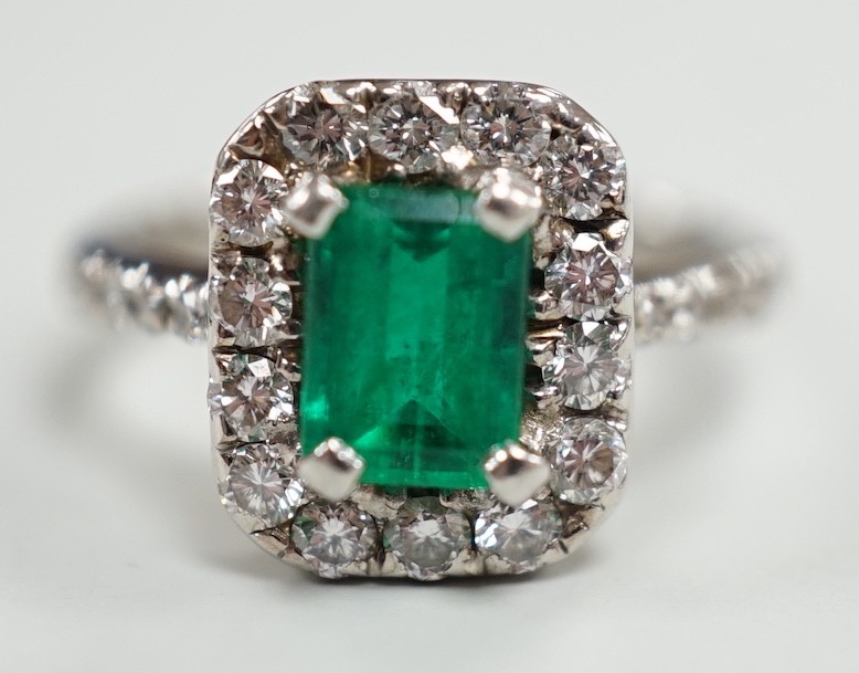 A modern 750 white metal, emerald and diamond set octagonal cluster ring, with diamond set shoulders, size J, gross weight 4.9 grams.